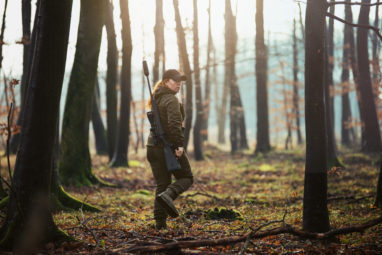 Jägerin mit Waffe im Wald auf dem Weg zur Jagd